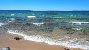 A beach with clear water and a distant island. - Lk Michigan Escape: Sunsets, Fireplace, Wine Trail (Lake Leelanau)