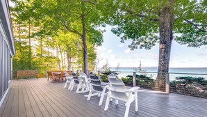 A wooden deck with white Adirondack chairs and a wooden bench, overlooking a body of water. - Lk Michigan Escape: Sunsets, Fireplace, Wine Trail (Lake Leelanau)