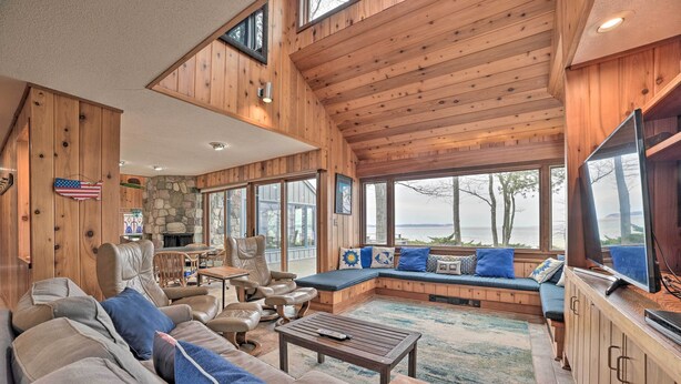 A cozy cabin interior with a stone fireplace, wooden walls, and large windows overlooking a lake. - Lk Michigan Escape: Sunsets, Fireplace, Wine Trail (Lake Leelanau)