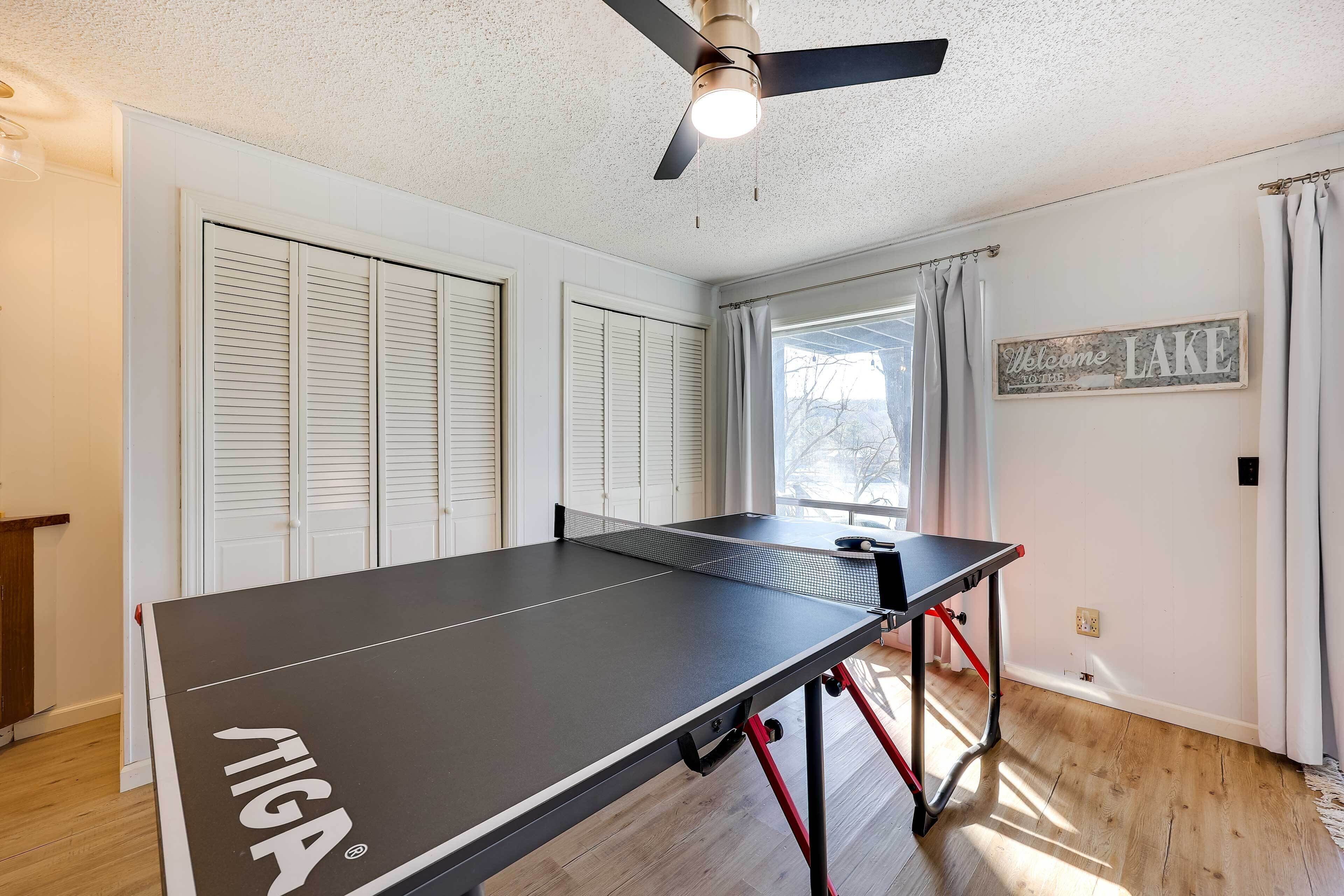 A ping pong table in a room with wooden flooring, white walls, and a ceiling fan.