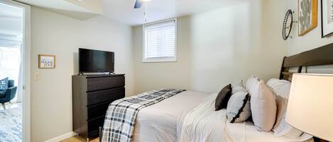 A bedroom with a bed, a television, a ceiling fan, and a window with blinds.