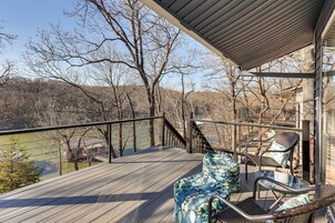 Une terrasse en bois, dotée de mobilier d’extérieur, d’une rambarde et offrant une vue sur une rivière et des arbres.
