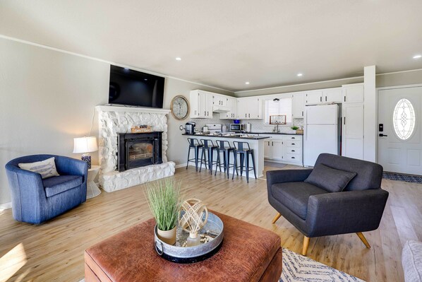 A modern living room with a fireplace, a kitchen with white cabinets, and a dining area with bar stools. - Deck, Dock, Fire Pit: Grand Lake Lakefront Home (Jay)