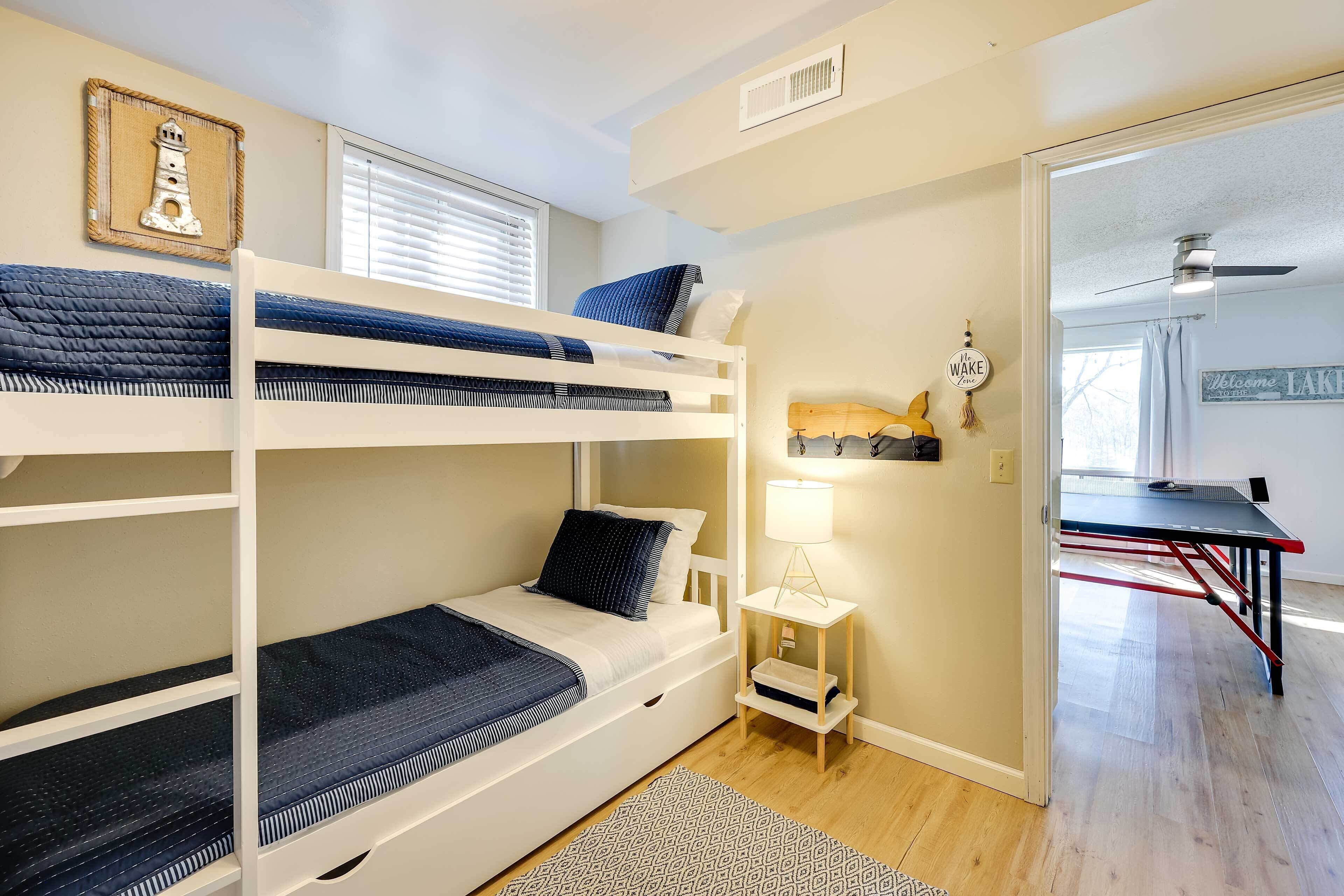 A bunk bed room with a small table and lamp, a framed picture on the wall, and a door leading to another room.