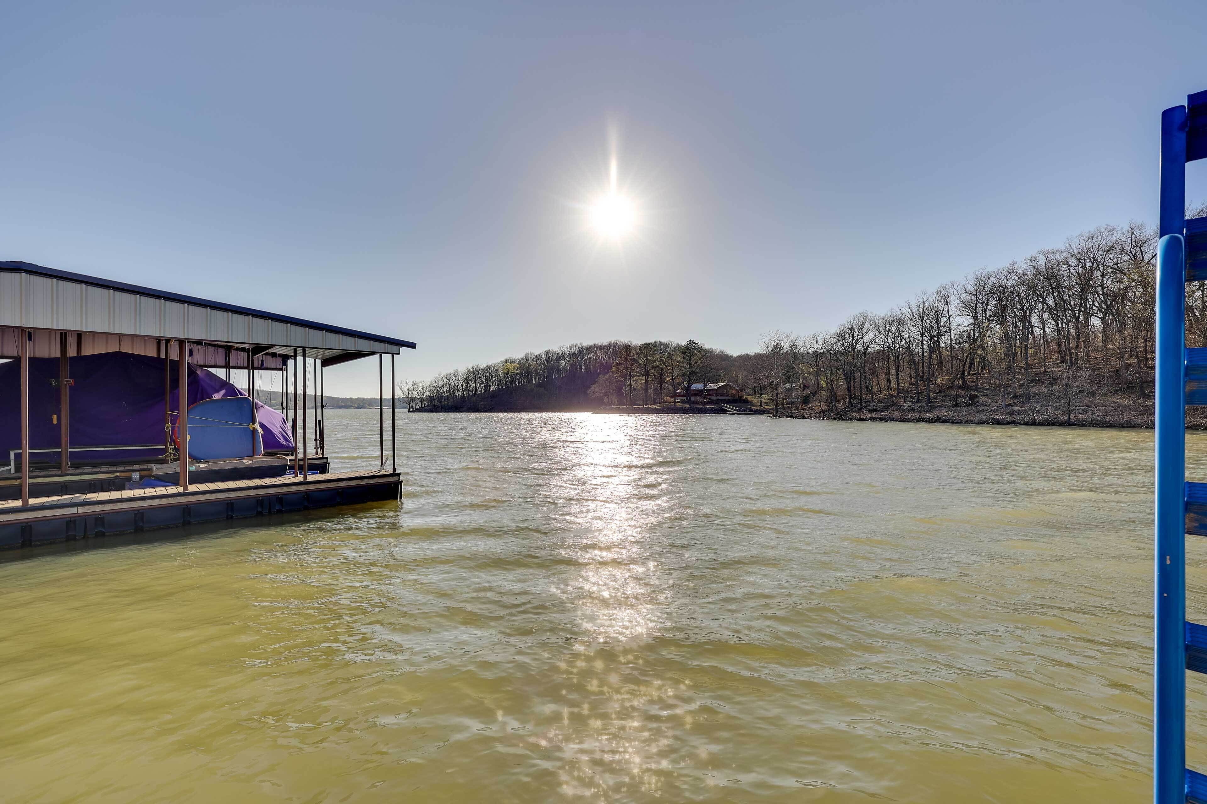 Ein Boot mit überdachtem Deck und einer kleinen Kabine liegt an einem ruhigen Fluss unter einem klaren Himmel, im Hintergrund ein bewaldeter Hügel.