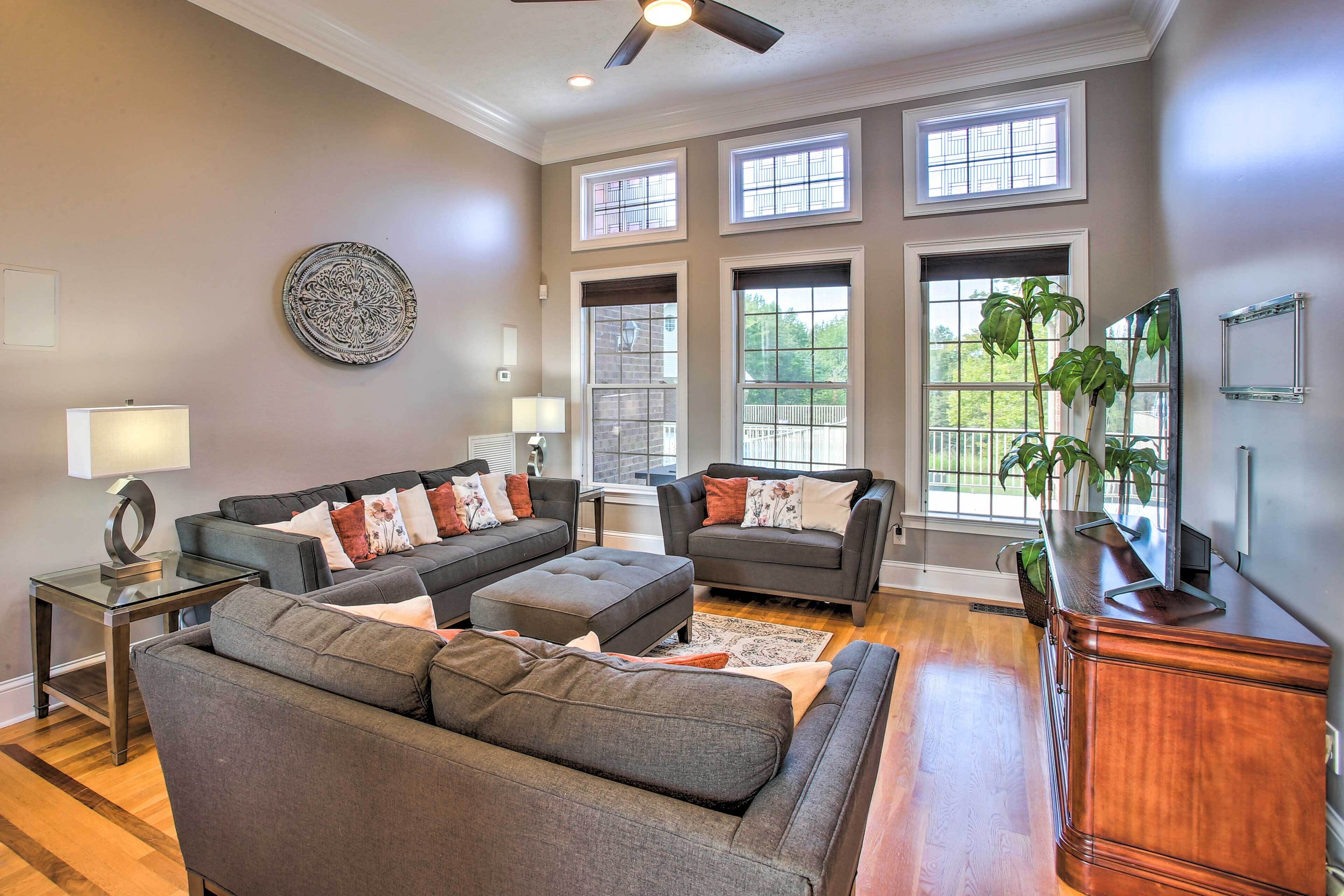 A spacious living room with grey sofas, a wooden coffee table, and a large window with a view of greenery.