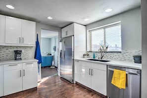 A modern kitchen with white cabinets, stainless steel appliances, and a window with blinds.
