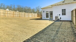 A fenced backyard with a white house, a covered patio, and a visible air conditioning unit. - Opelika Townhome w/ Central A/C + Heating! (Opelika)