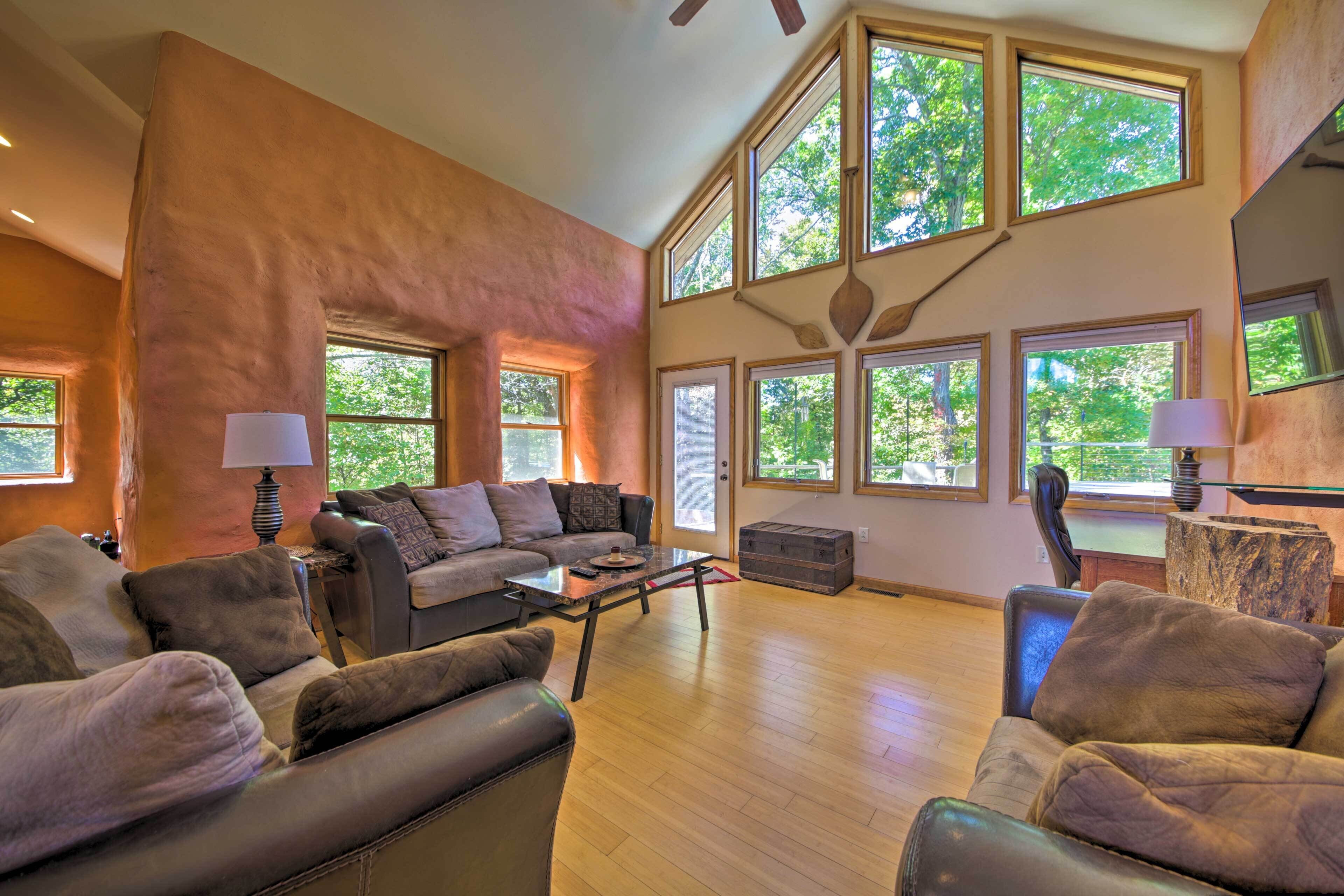 A spacious living room with a large sofa, a coffee table, and multiple windows offering a view of the outdoors.