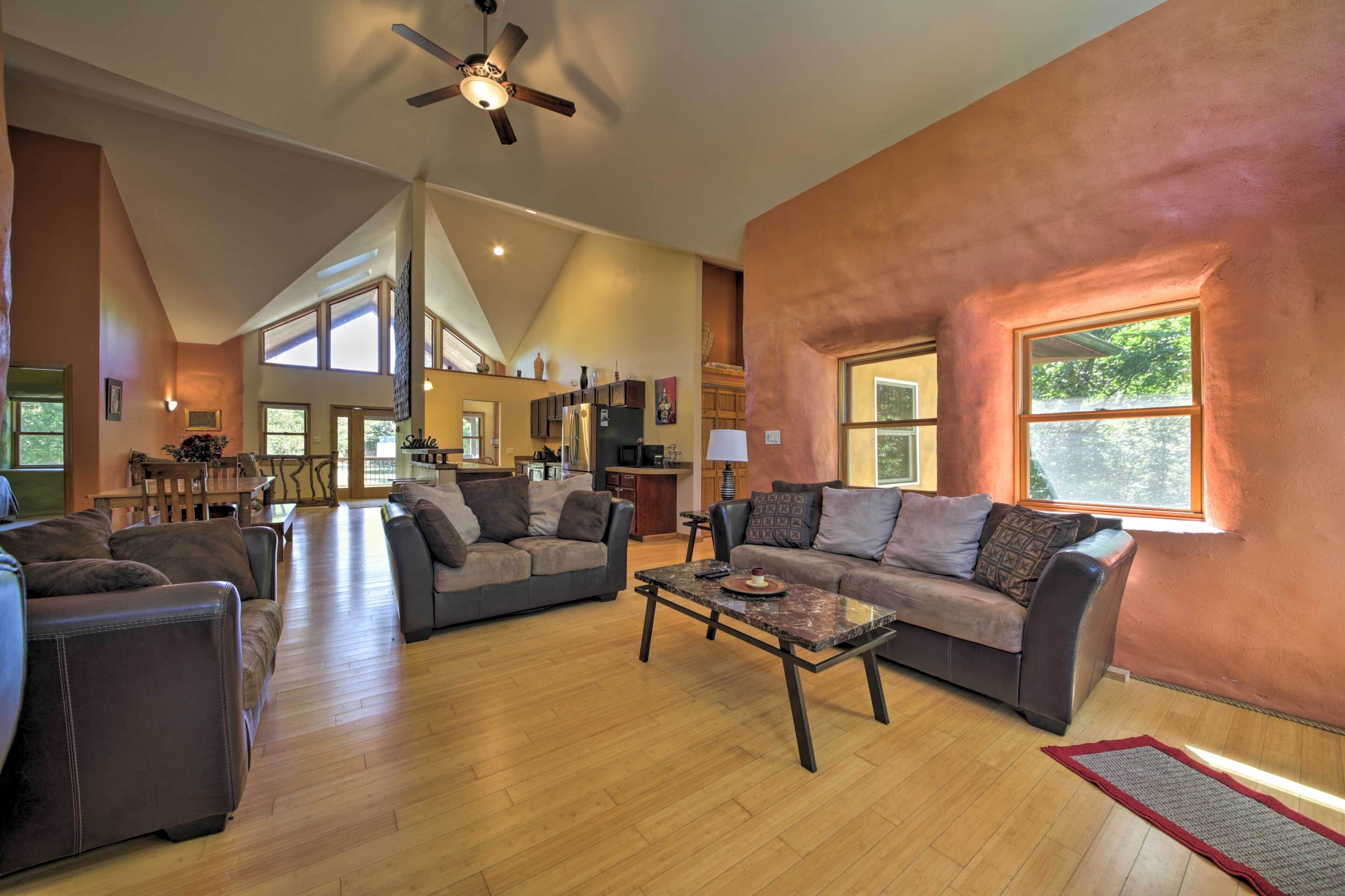 A spacious living room with a high ceiling, a ceiling fan, and a large window providing natural light.