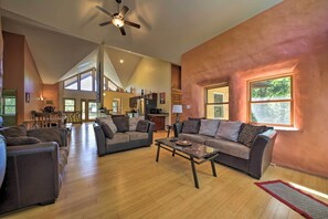 A spacious living room with a high ceiling, a ceiling fan, and a large window providing natural light.