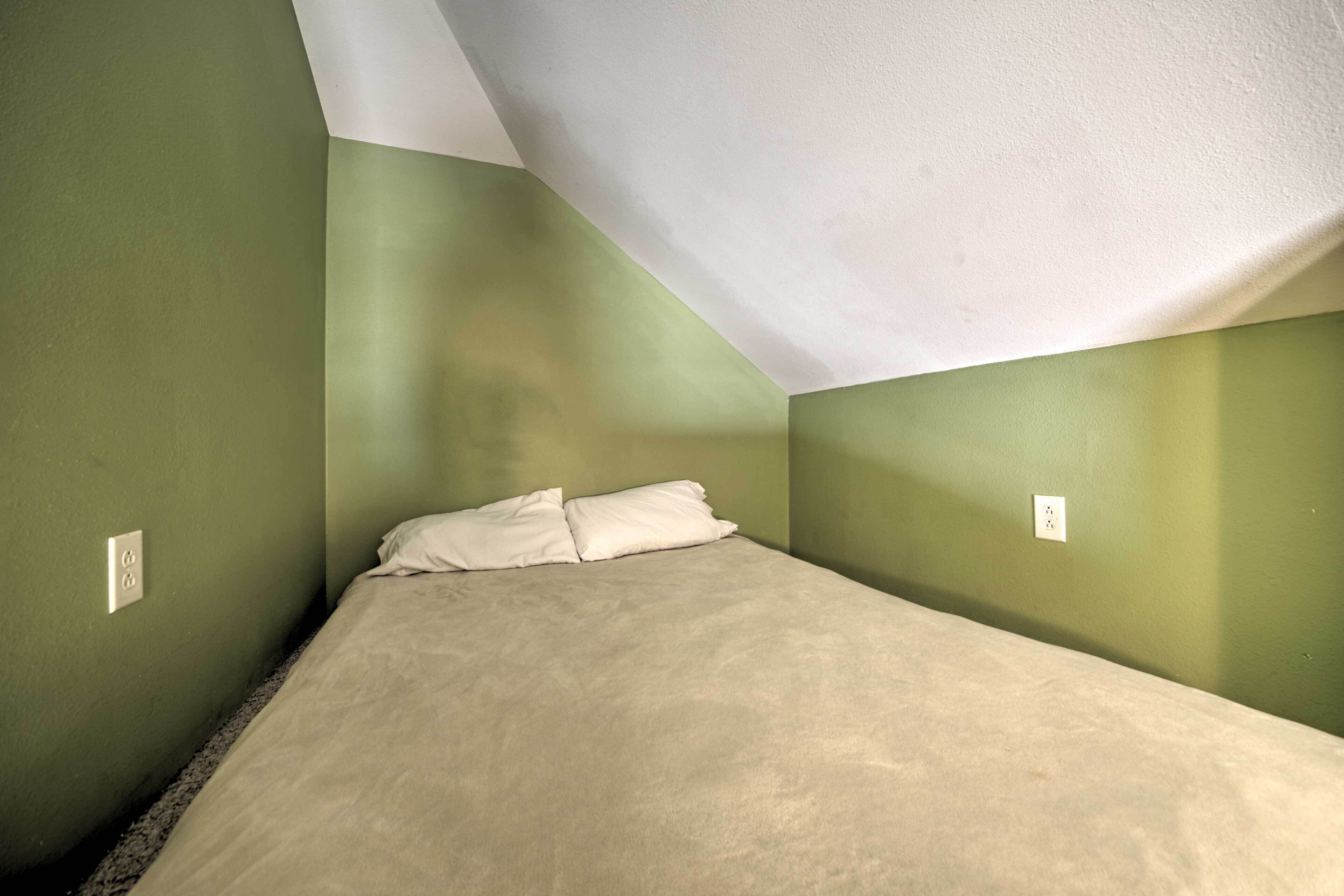 Una camera piccola con un letto singolo, pareti verdi e un soffitto spiovente.