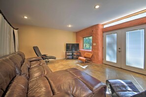 A spacious living room with a large leather sofa, a black armchair, and a television on a stand.