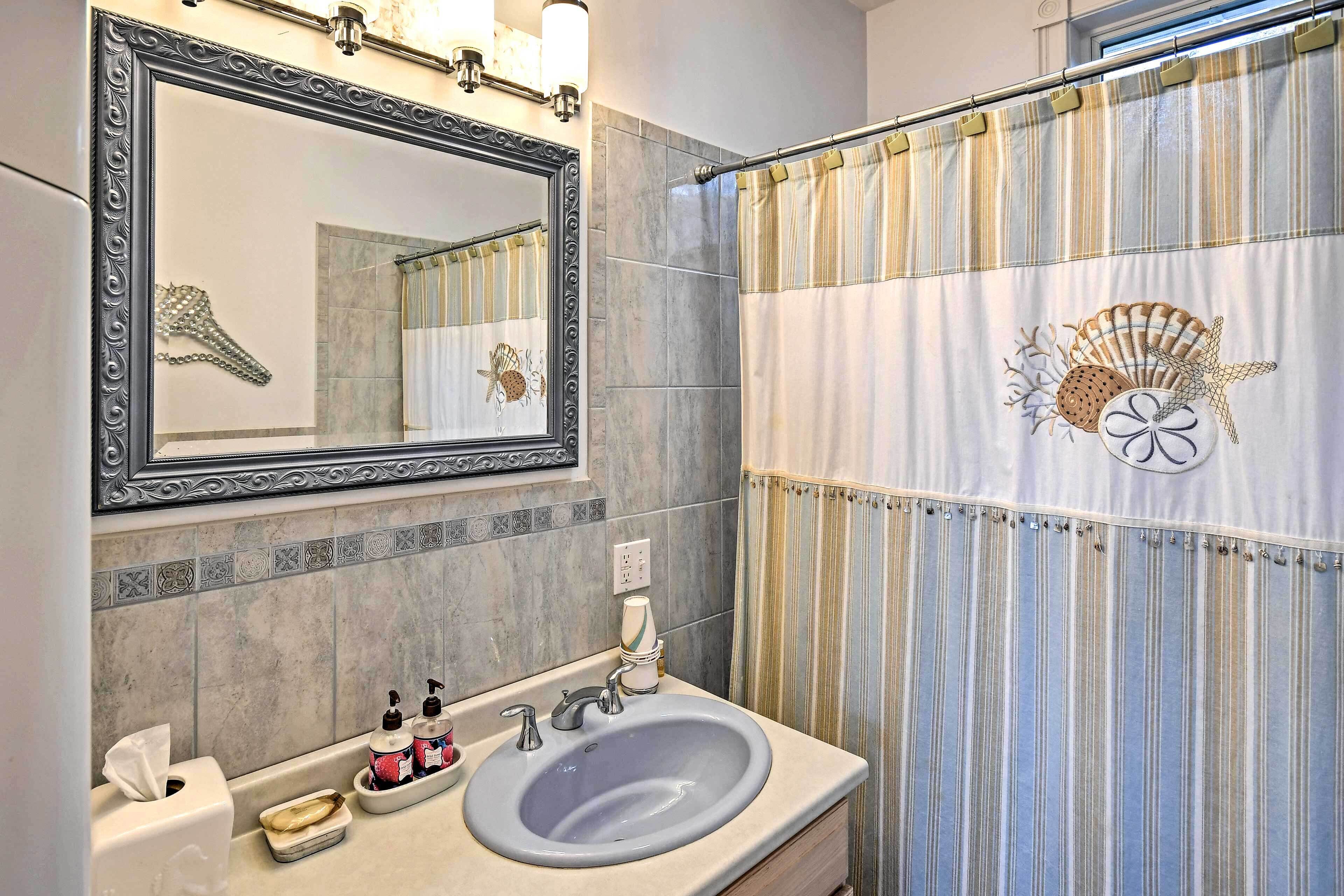 A bathroom with a large mirror, a sink, and a shower curtain with a seashell design.