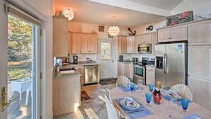 A modern kitchen with light wood cabinets, stainless steel appliances, and a dining area with a table set for four. - 2BR Coastal Gem! Breathtaking Ocean/mountain View (Sullivan)
