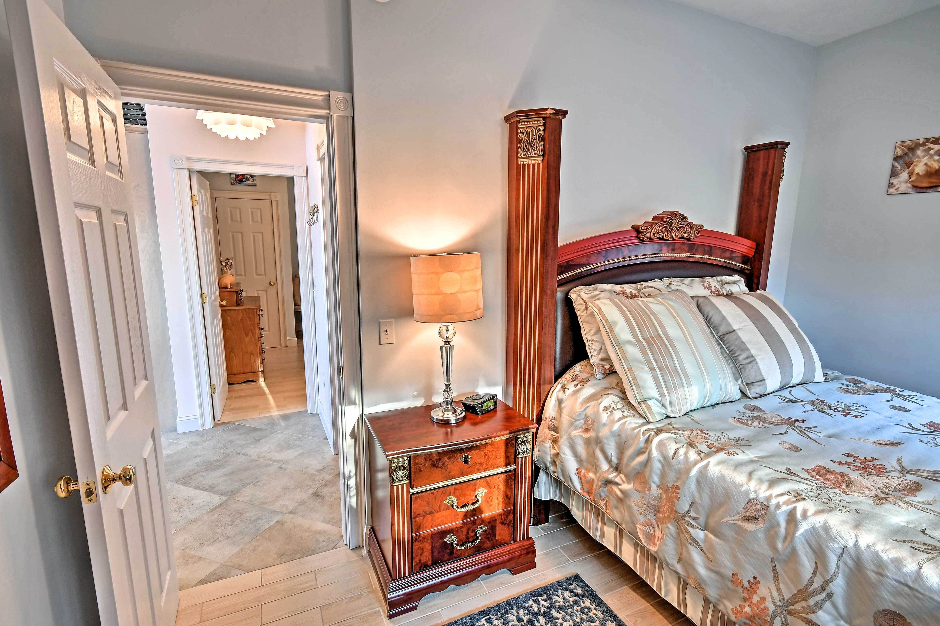 Un dormitorio con cama, mesita de noche, lámpara y una puerta que da a otra habitación.
