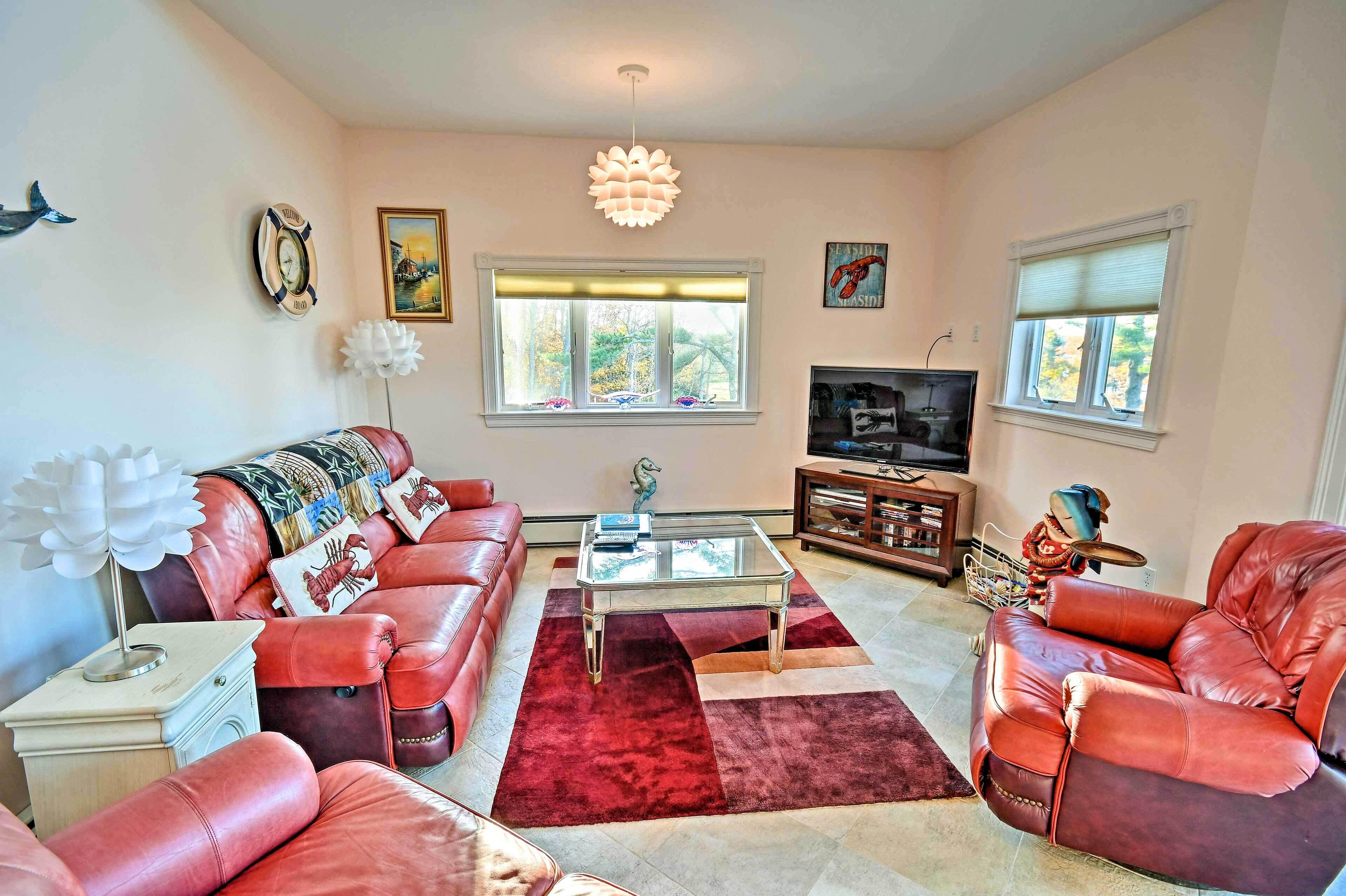 A living room with red leather sofas, a glass coffee table, a red rug, a television, and a window with blinds.