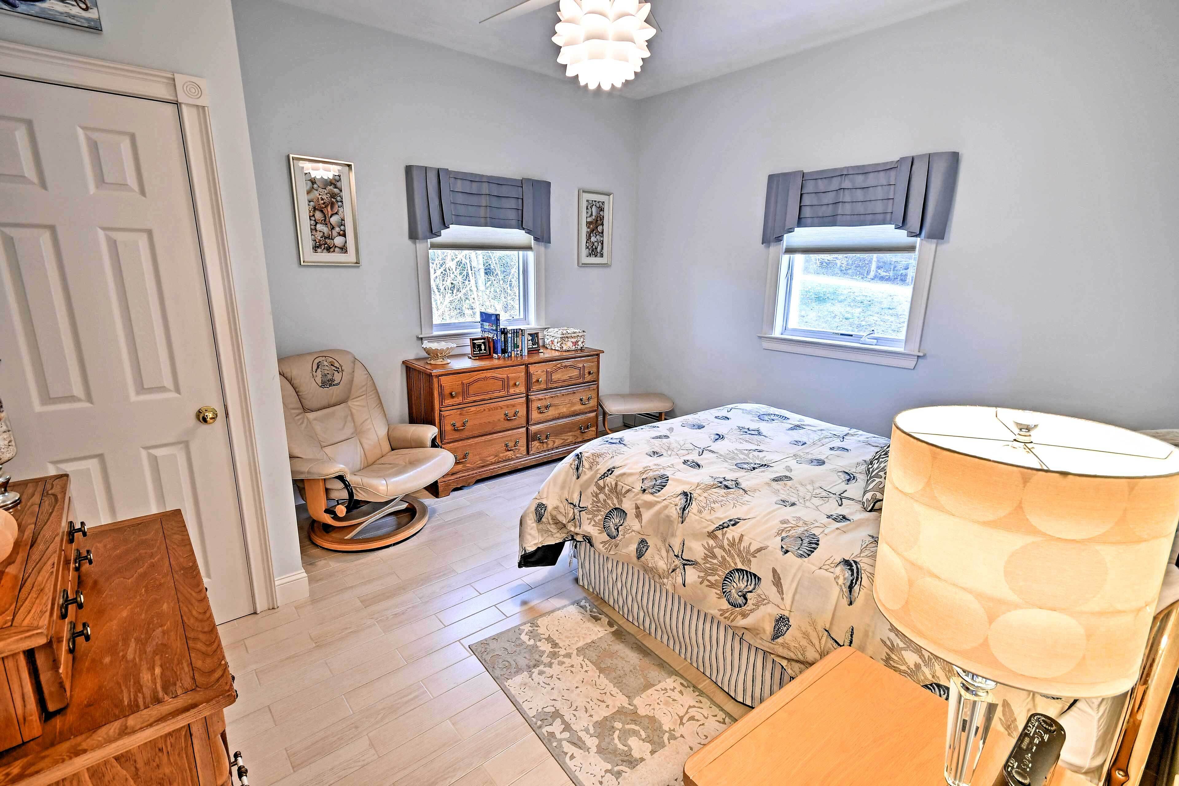 A bedroom with a bed, dresser, chair, and a lamp.