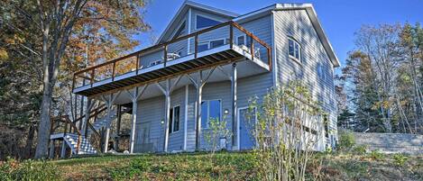 A two-story house with a balcony, surrounded by trees and a grassy area.