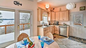 A kitchen with wooden cabinets, a dining area with a table set for two, and a view of the outdoors. - 2BR Coastal Gem! Breathtaking Ocean/mountain View (Sullivan)