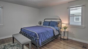 Ein Schlafzimmer mit einem Metallbettgestell, einer blauen Bettdecke, einem Nachttisch mit einer Lampe und einem Fenster mit Jalousien.