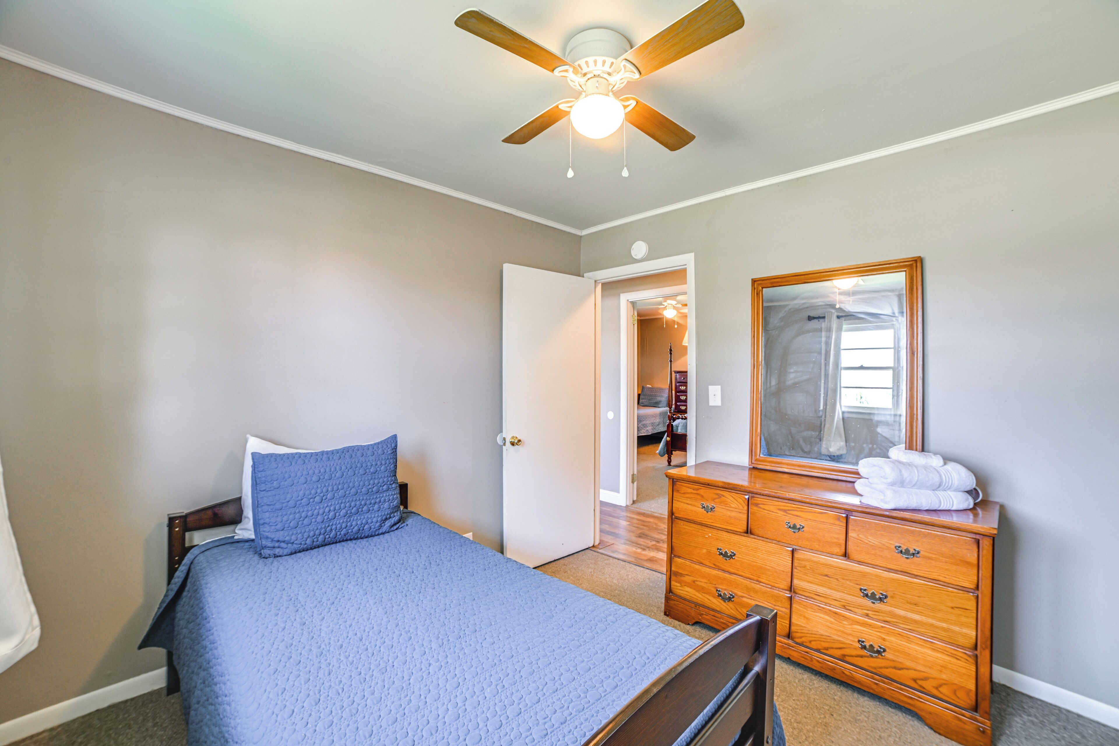 A bedroom with a bed, a dresser, a ceiling fan, and a door leading to another room.