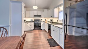 A modern kitchen with white cabinets, stainless steel appliances, and a wooden dining table. - Walkable Sodus Point Retreat < 1 Mi to Lake (Sodus Point)