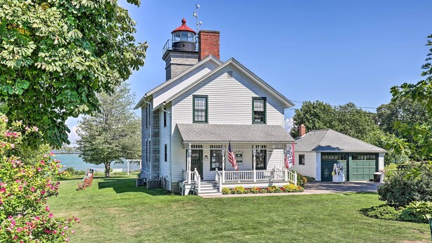 A white two-story house with a red-roofed tower, a front porch with a railing, and a garage. - Walkable Sodus Point Retreat < 1 Mi to Lake (Sodus Point)