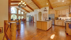 Una cocina amplia con armarios de madera, una isla central y un comedor con techo alto y ventanas grandes.