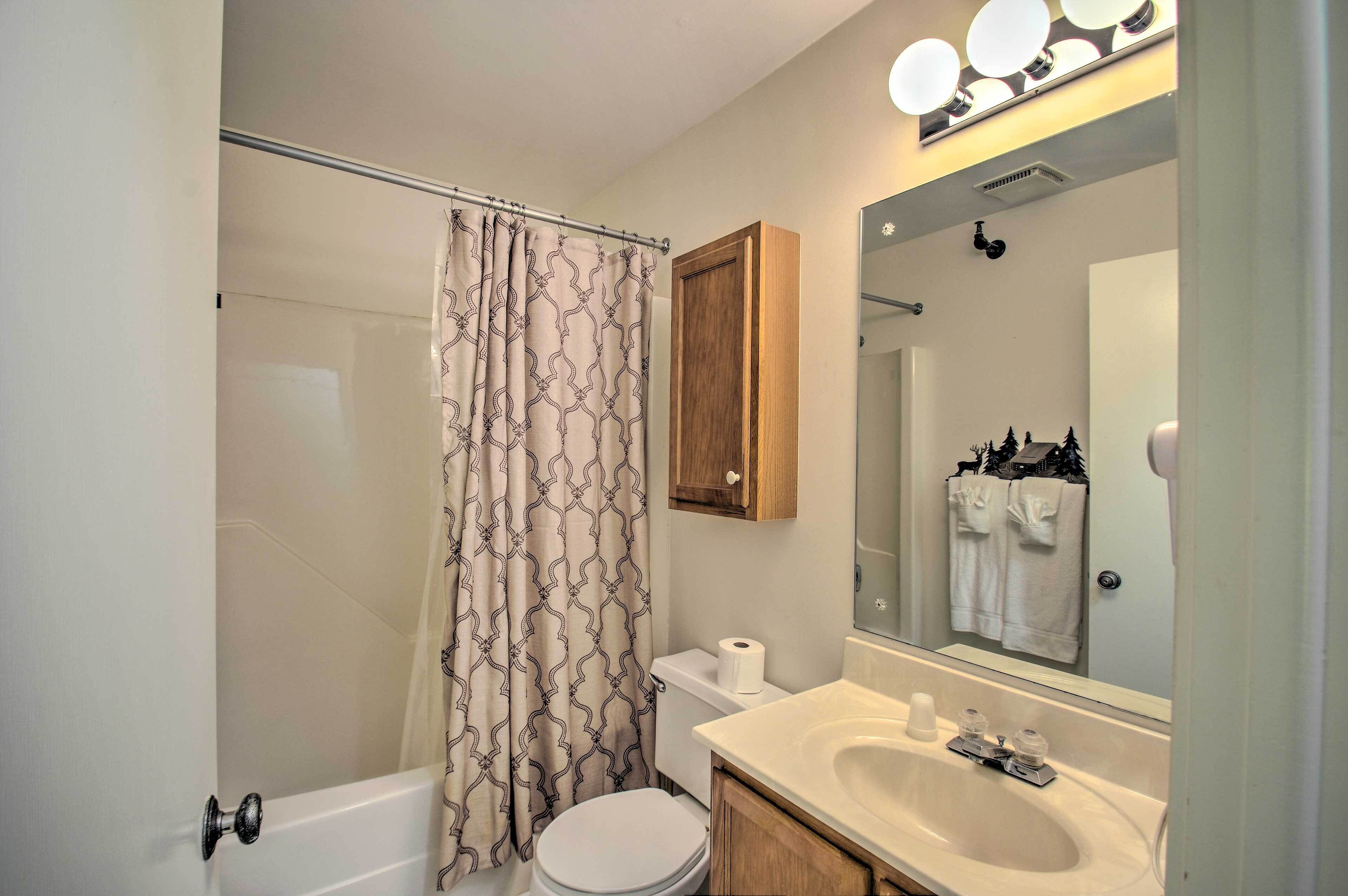 A bathroom with a shower, toilet, sink, and a mirror with lights above.