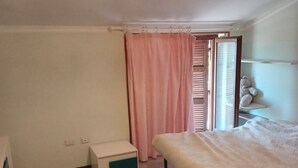 A bedroom with a bed, a bedside table, a hanging light fixture, a window with blinds, and a pink curtain. - PANORAMIC VILLA (Bagnoregio)