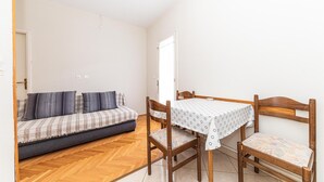 Une petite pièce agréable et chaleureuse, avec un canapé, une table à manger en bois et des chaises, et un parquet en bois disposé en motif chevrons.