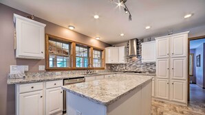 A kitchen with white cabinetry, a granite countertop, and a large island. - Spacious Lakefront Home w/ Sunroom & Bar! (Rogers City)