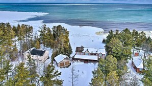 A snow-covered landscape with a large house surrounded by trees, near a body of water. - Spacious Lakefront Home w/ Sunroom & Bar! (Rogers City)