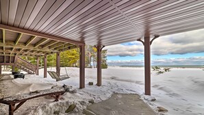 A covered outdoor area with a wooden deck, a swing, and a view of the beach. - Spacious Lakefront Home w/ Sunroom & Bar! (Rogers City)