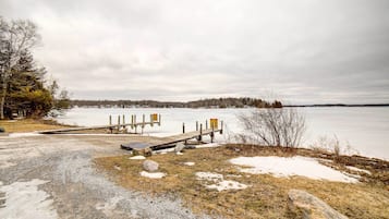 A snowy landscape with a dock extending into a frozen lake, surrounded by trees and a cloudy sky.