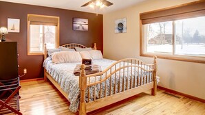 A bedroom with a wooden bed, a ceiling fan, and a window with a view of a snowy landscape. - Waterfront Evart House on Chippewa Lake Channel (Evart)