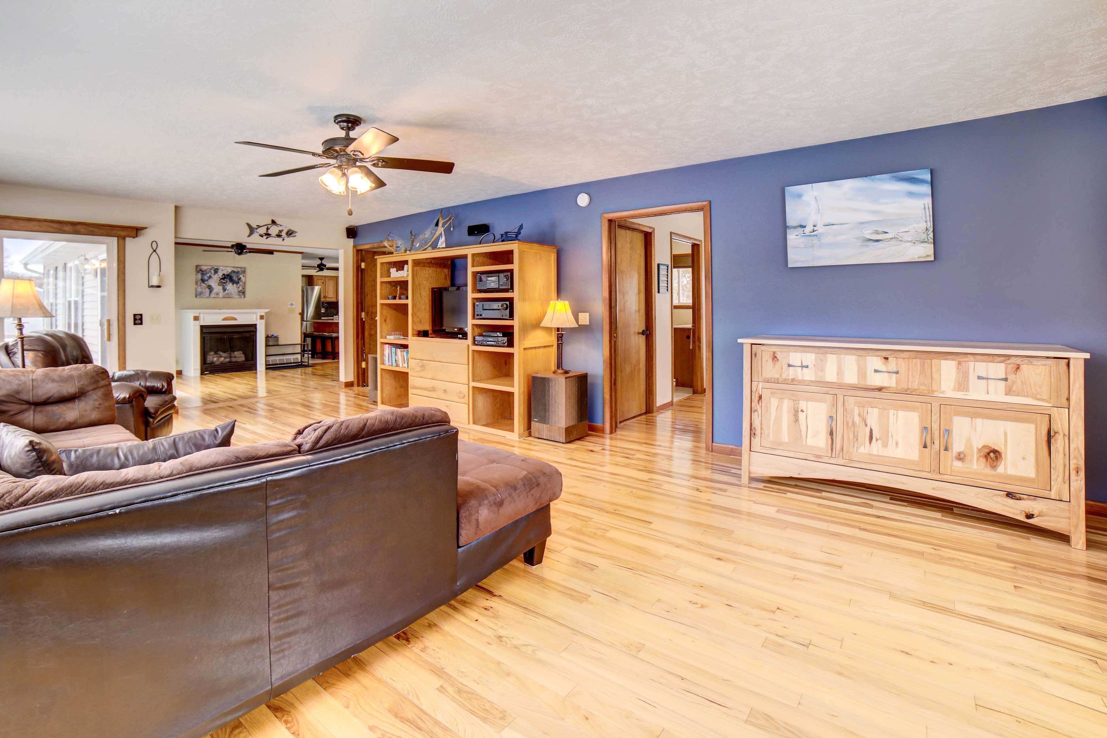 A spacious living room with a brown leather sofa, wooden flooring, a ceiling fan, and a wooden cabinet.