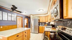 A kitchen with wooden cabinets, a stainless steel refrigerator, a black stove, and a ceiling fan. - Waterfront Evart House on Chippewa Lake Channel (Evart)
