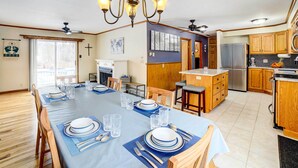 A spacious kitchen with wooden cabinets, a stainless steel refrigerator, and a dining area set for a meal. - Waterfront Evart House on Chippewa Lake Channel (Evart)