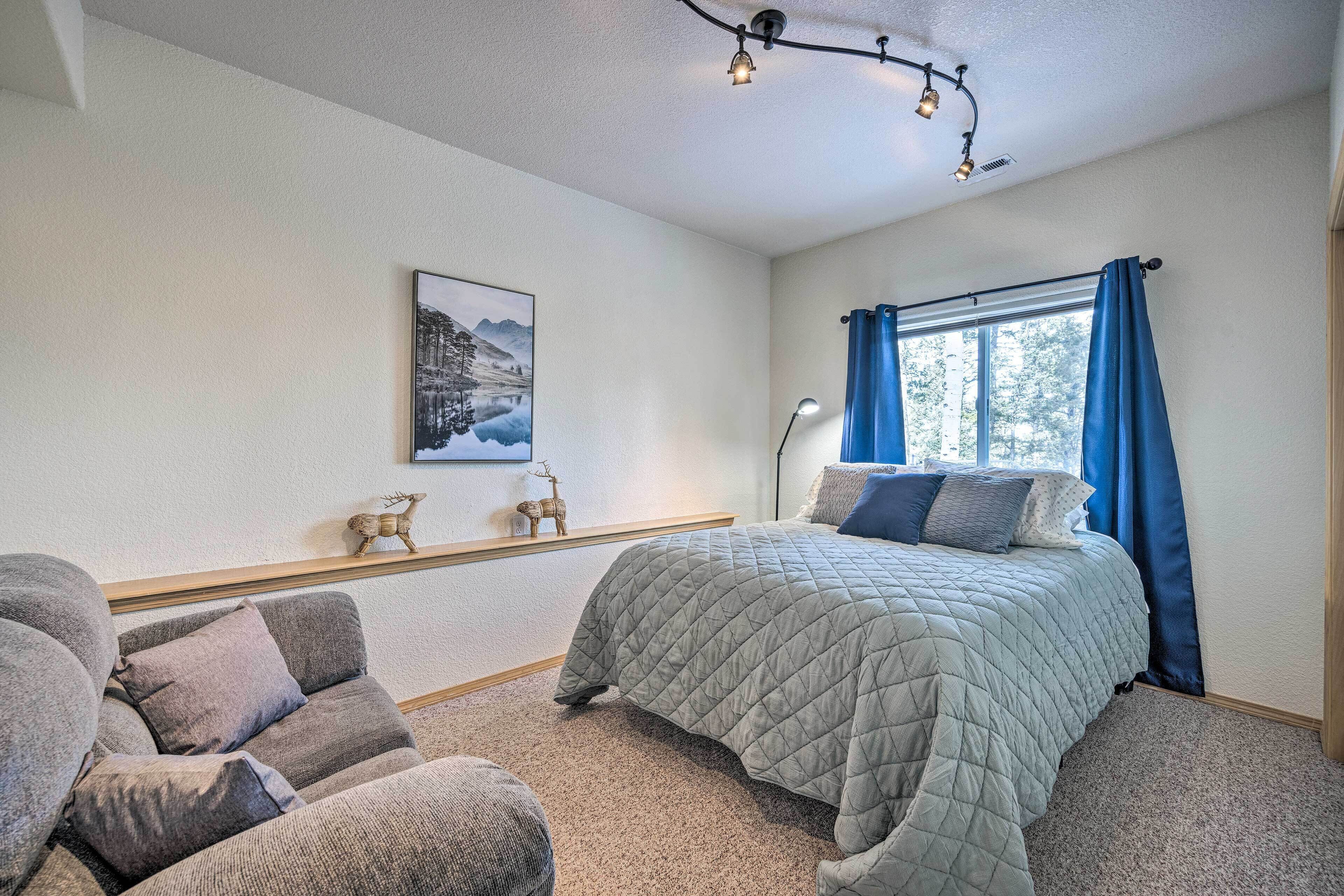 Um quarto com cama, sofá, janela com cortinas, luminária e quadro na parede.