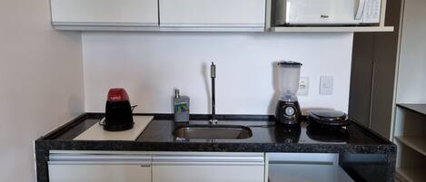 Una cucina compatta con un forno a microonde bianco, una macchina da caffè, un frullatore e un piccolo frigorifero.