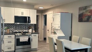 A modern kitchen with white cabinets, stainless steel appliances, and a dining area with a white table and chairs. - Cozy Retro Downtown Living (Albuquerque)