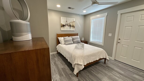A bedroom with a bed, a white ceiling fan, a painting of the Eiffel Tower, a window with blinds, and a white door. - Cozy Retro Downtown Living (Albuquerque)