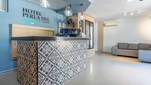 A hotel reception area with a patterned tile wall, a reception desk, a sofa, and pendant lighting. - Hotel Perla Del Caribe (Santa Marta)