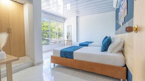 A modern bedroom with a large bed, wooden wardrobe, and a view of greenery outside. - Hotel Perla Del Caribe (Santa Marta)
