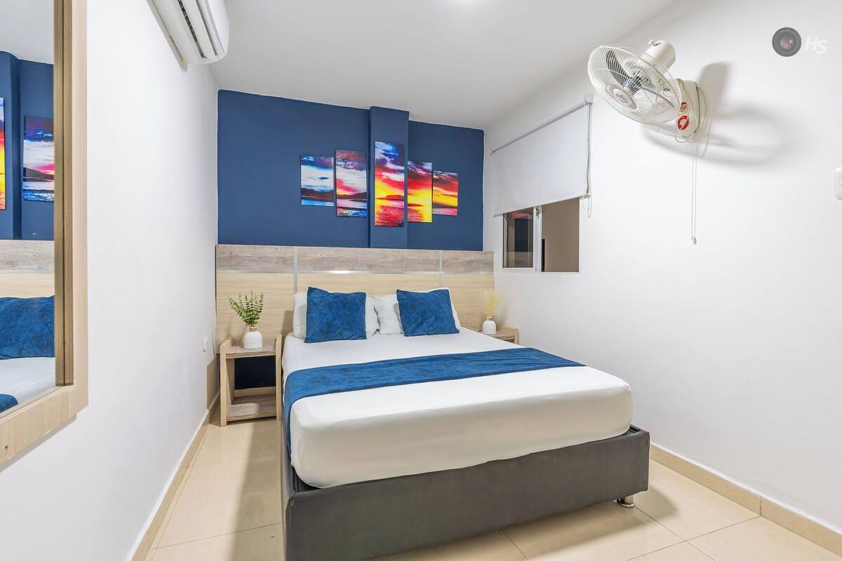 Une chambre d’hôtel moderne équipée d’un lit, d’une table de chevet, d’une petite table, d’un climatiseur fixé au mur et d’un ventilateur de plafond.