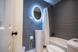 A bathroom with a white sink, a round mirror, a toilet, and a bathtub.