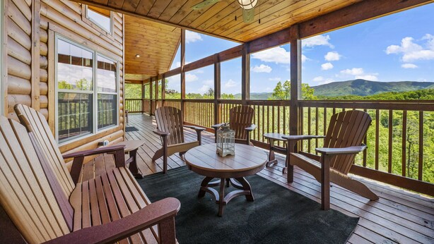 Una terraza de madera con sillas tipo Adirondack, una mesa redonda y un farol.