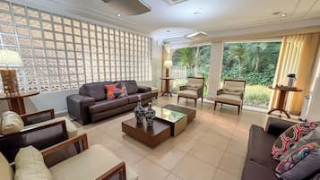 A spacious living room with a brown sofa, two armchairs, a coffee table, and a decorative wall panel.
